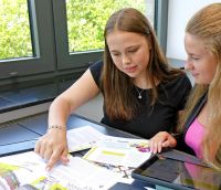 Zwei junge Frauen sitzen an einem Tisch und schauen gemeinsam auf Unterlagen